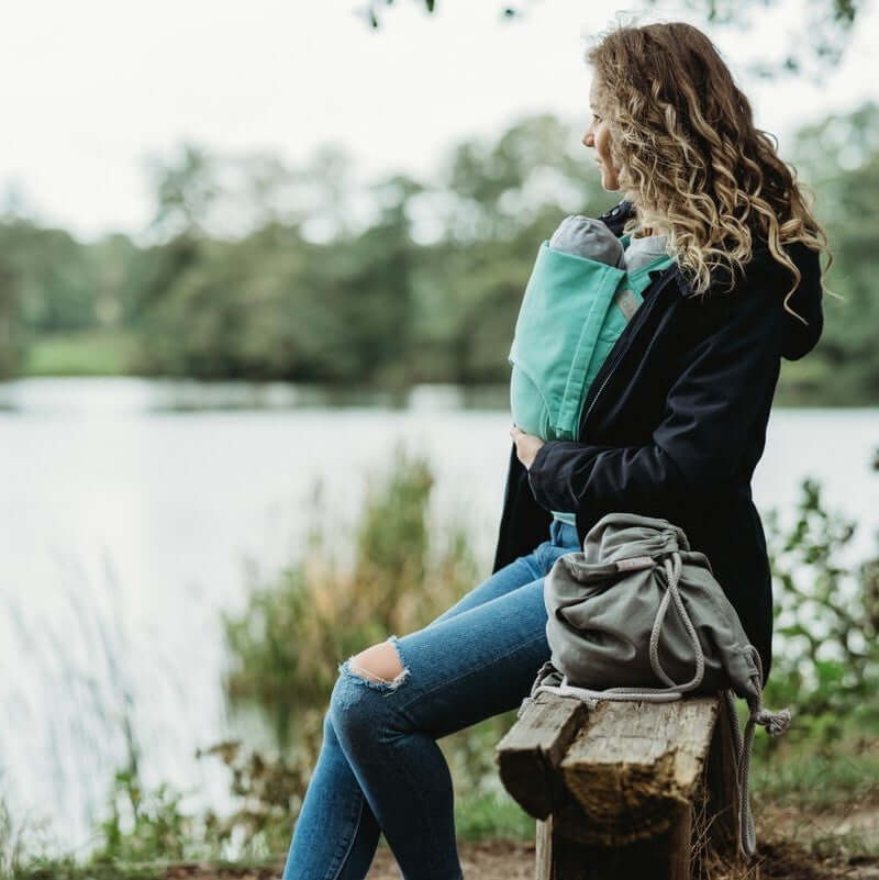 Woman wearing Wombat & Co. London - Wallaby Maternity & Babywearing Coat - Navy while babywearing by a lake | Babymaxi