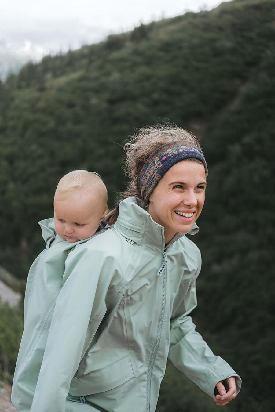 Mom wearing Mamalila Explorer Outdoor Baby Carrier Jacket - Mint while hiking with baby, ensuring weather protection | Babymaxi