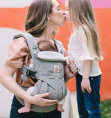 A mother uses the Ergobaby Omni Classic Cotton Carrier - Pearl Grey to hold her baby while sharing a kiss with her toddler | Babymaxi