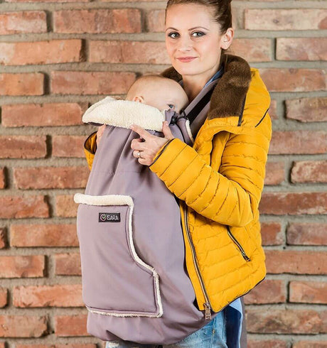 Woman wearing the Isara Winter Baby Carrier Cover - Frosted Almond Taupe with baby, cozy style for cold weather | Babymaxi
