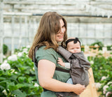 Mom joyfully carrying baby in Neko Switch Baby Carrier - Bold, 2 extra hoods in a lush garden setting | Babymaxi