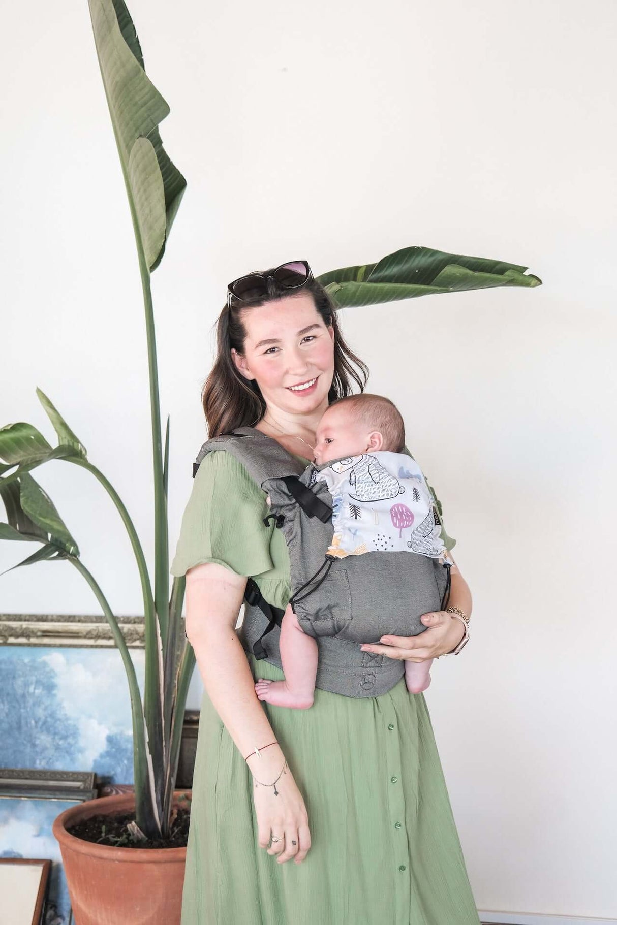 Mom holding baby in Neko Switch Baby Carrier - Bold, 2 extra hoods with plant in background | Babymaxi