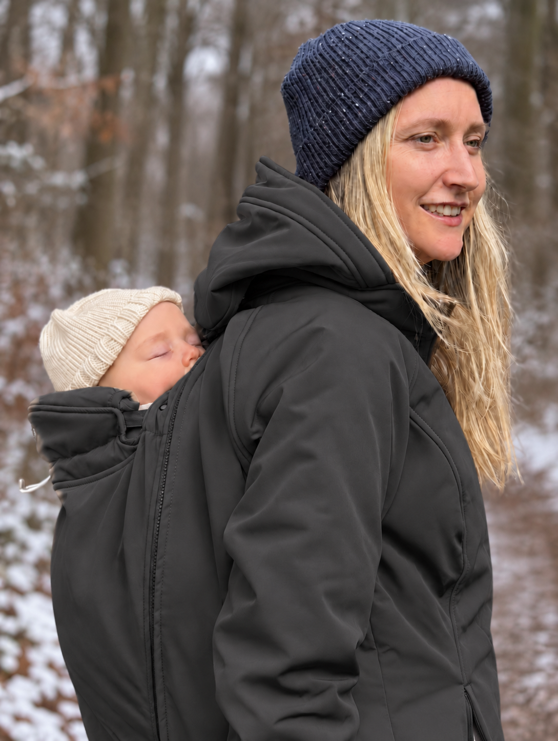 Mamalila Allrounder Winter softshell babywearing jacket in black, mum carrying her baby on her back on a snowy walk